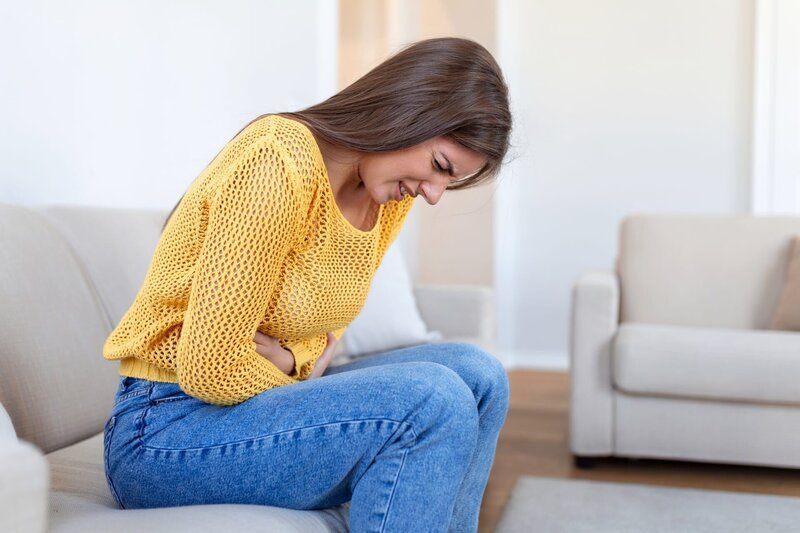 Stockfotografie Frau liegt krank auf Sofa im Wohnzimmer. Schöne junge Frau auf dem Bett liegend und Händchen haltend auf dem Bauch. Frau mit schmerzhaften Bauchschmerzen im Bett, Menstruationszeit: lizenzfreie Fotos – Bild: depositphotos