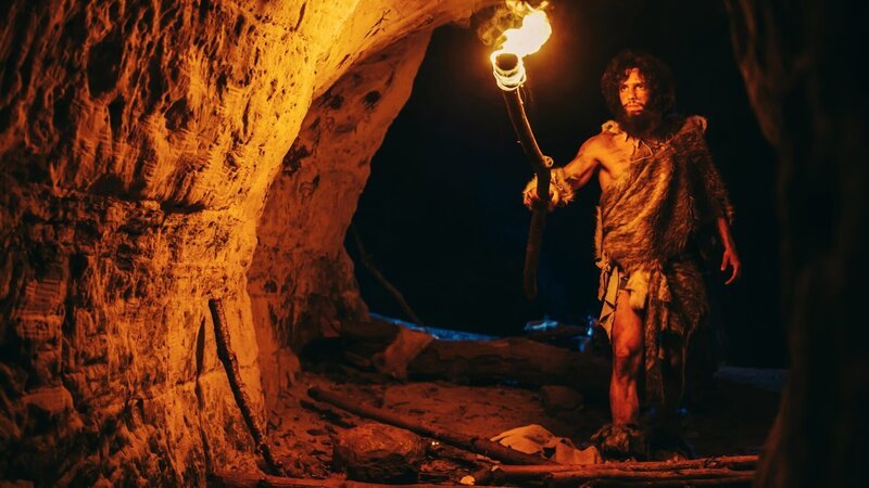 Stockfotografie Ur-Höhlenmensch in Tierhaut erkundet nachts die Höhle, hält eine Fackel mit Feuer in der Hand und betrachtet nachts Zeichnungen an den Wänden. Neandertaler auf der Suche nach sicherem Übernachtungsplatz: lizenzfreie Fotos – Bild: depositphotos