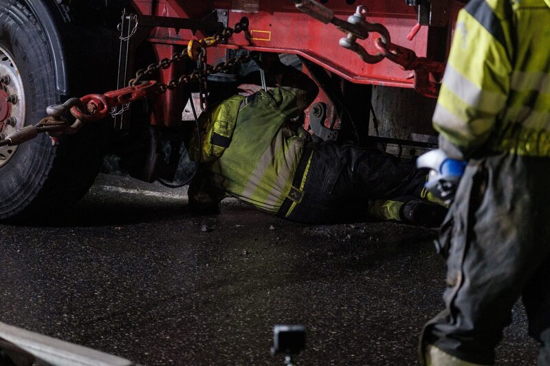 Thord krabbelt unter den Lkw, um Kisten zu platzieren, die den Lkw und den Anhänger aus dem Graben ziehen. – Bild: National Geographic/​Gullhaugveien