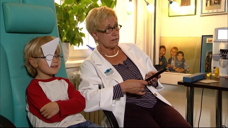 Feris bei der Augenärztin. Sie schaut nach, ob die neuen Brillen auch die richtige Stärke haben. – Bild: WDR/​Die Sendung mit dem Elefanten