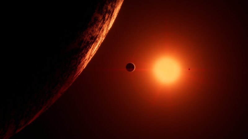 Trappist 1 ist ein Roter Zwerg. Er hat nur 10 Prozent der Masse der Sonne und 1 Prozent ihrer Helligkeit. Sein rotes Licht erhellt schwach seine sieben erdgroßen Planeten. – Bild: BBC Studios