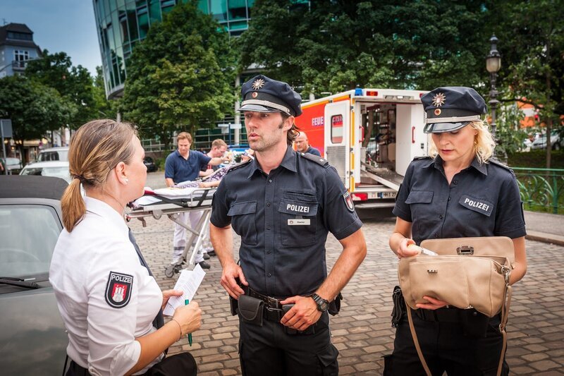 Während Mattes (Matthias Schloo) mit der Politesse (Komparsin, l.) spricht, die die bewusstlose Frau im Auto gefunden hat, durchsucht Melanie (Sanna Englund, r.) deren Handtasche nach Ausweispapieren. – Bild: Boris Laewen