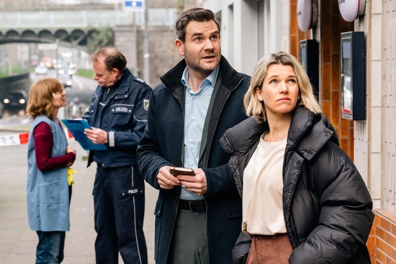 Die Kommissare Jonas Fischer (Lukas Piloty) und Vanessa Haas (Kerstin Landsmann) stehen vor der gemütlichen, Kölschen Eckkneipe „Im Krügchen“, die in der vergangenen Nacht zum finsteren Tatort wurde. – Bild: Martin Rottenkolber /​ ZDF