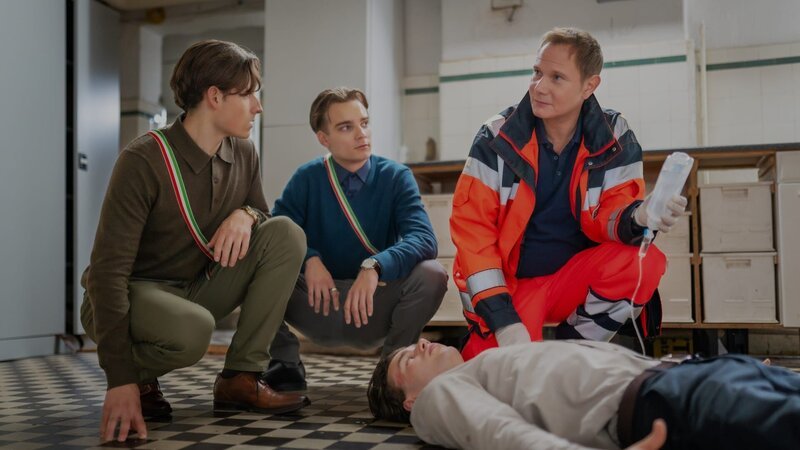 Dr. Haase (Fabian Harloff, r.) kommt gerade noch rechtzeitig, um Schlimmeres zu verhindern. Maximilians (Valentin Oppermann, liegend) Verbindungskameraden Nicolas (Moritz Bäckerling, l.) und Marvin (Mateo Wansing Lorrio, 2.v.l.) behaupten, nicht zu wissen, was vorgefallen ist. – Bild: Boris Laewen /​ ZDF