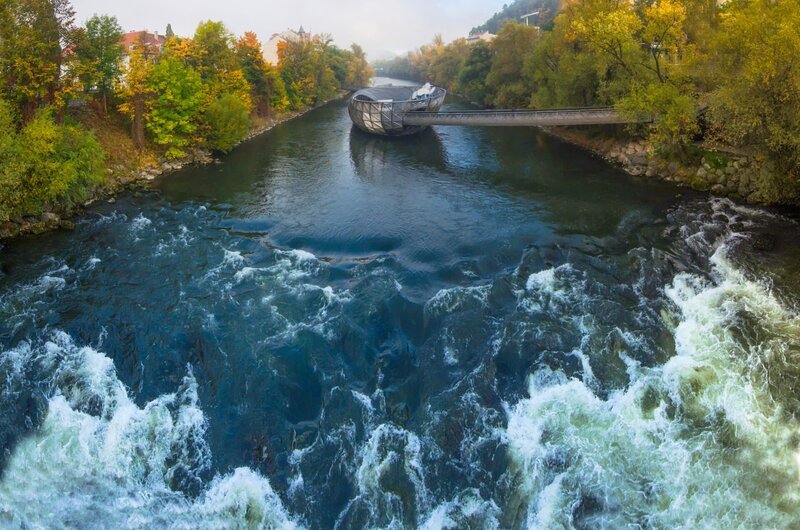 Mur river in autumn, with Murinsel bridge and old buildings in the city center of Graz, Styria region, Austria. – Bild: Shutterstock /​ Aron M