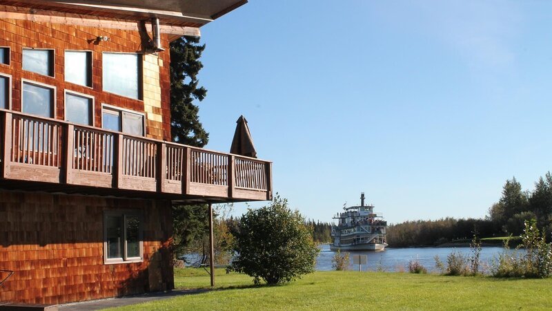 Exterior, side of house with wrap around deck, backyard leads to rivers edge, riverboat moving by, one of the stops in the Greenwoods house search, Chena River house, Fairbanks, Alaska, as seen on Great American Country’s Living Alaska – Bild: Great American Country/​Scripps Networks, LLC.