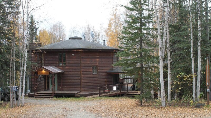 Exterior, octagon shaped house with wood siding, The Folk School wood sign hanging above door, wrap around porch to other house, on one of the stops in the Keeney family house search, Eton Boulevard, Fairbanks, Alaska, Great American Country’s Living Alaska. – Bild: Great American Country/​Scripps Networks, LLC