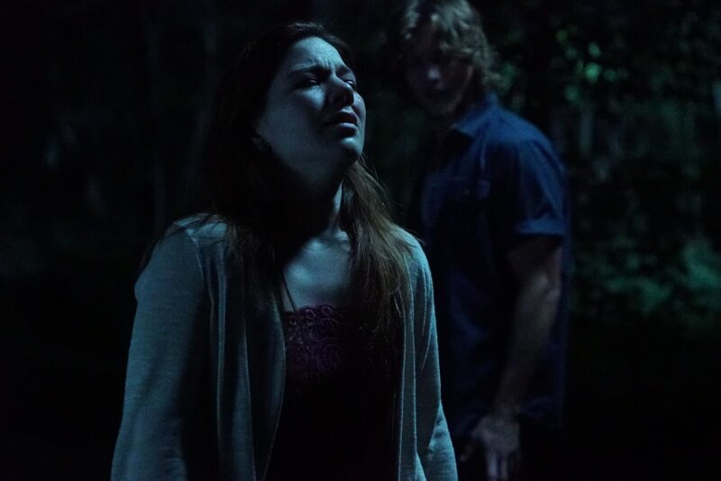 A young woman cries in a dark woods while a young man stands in the background. – Bild: Discovery Communications