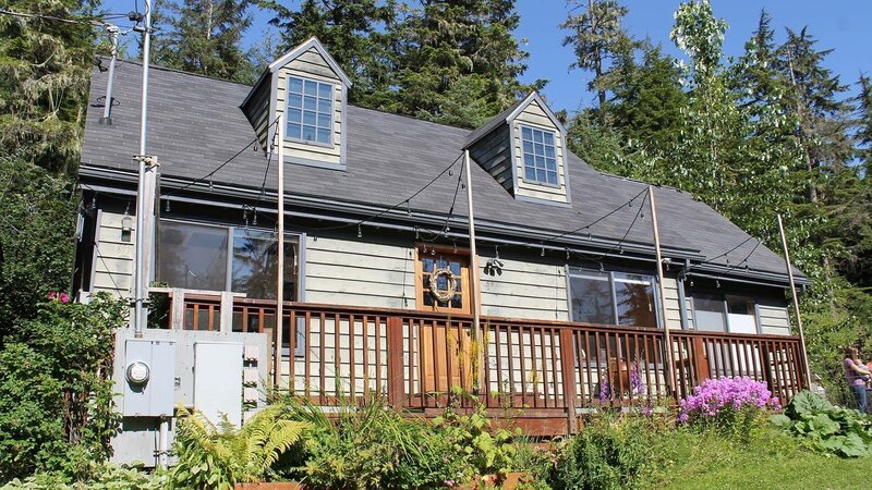 Exterior, house, at Cove House, complete with front porch, grey siding, surrounded by trees, near Juneau, Alaska, as seen on Great American Country’s Living Alaska – Bild: Great American Country/​Scripps Networks, LLC
