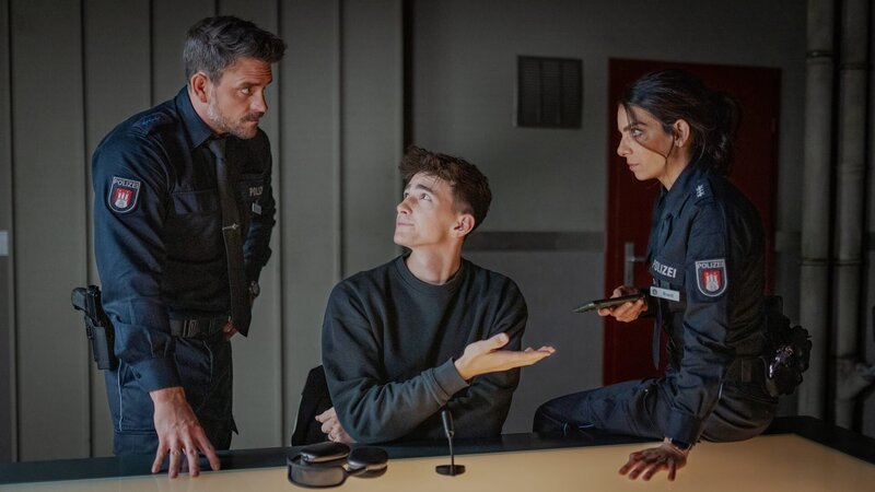 Nach intensiver Befragung durch Kris (Marc Barthel, l.) und Isa (Lilli Hollunder) überlässt Johannes Berendsen (Nathan Goldblat, M.) widerwillig der Polizei seine Social Media-Aufnahmen. – Bild: Boris Laewen