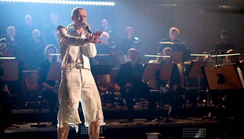 Mit seiner Version der WM-Hymne von Herbert Grönemeyer hat Soho Bani (Foto) ein politisches Statement für die Gegenwart gesetzt und damit auch den ersten Platz der deutschen Charts erreicht. Er erzählt von den Missständen, Ängsten und Sorgen, die ihn und seine Freunde beschäftigen, und warum er mit seiner Musik eine Message vermitteln will. Seine Performance mit dem MDR-Sinfonieorchester wird vom MDR-Rundfunkchor begleitet. – Bild: WDR/​ARD Kultur Midflight/​Samantha Gluth