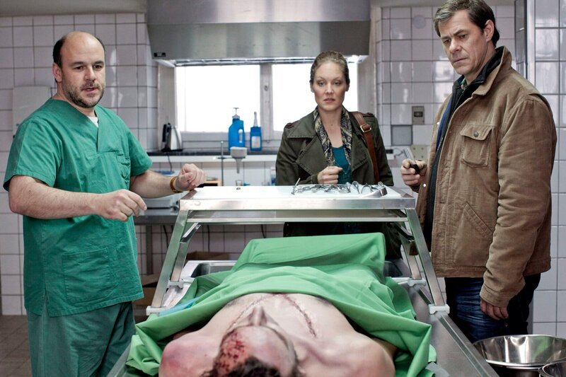 Im Lübecker Industriegebiet am Hafen wird die Leiche des Schauspielers Roland Freesmann gefunden. Pathologe Strahl (Christoph Tomanek, l.) erklärt Finn Kiesewetter (Sven Martinek, r.) und Elke Rasmussen (Tessa Mittelstaedt, M.) die Ergebnisse seiner Untersuchungen. – Bild: MDR/​Georges Pauly