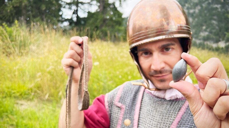 einstein Mit dieser tödlichen Waffe eroberte das Römische Reich die Schweiz Moderator Tobias Müller zeigt in römischer Ausrüstung das Schleuerblei – Bild: SRF