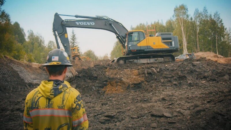 Ein Mann beobachtet einen Bagger bei der Arbeit. – Bild: Warner Bros. Discovery