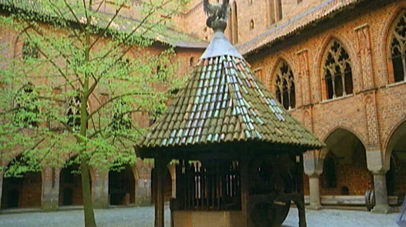 Ein Innenhof der Burganlage von Burg Malbork mit gotischen Stilelementen an Fassade und Brunnen. – Bild: BR/​SWR