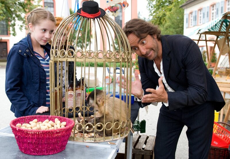 Greta (Enya Elstner, li.) und Celine (Zora Achtnich, re. neben ihr) bringen die Möbelpolitur zurück zum Stand von Famula (Dieter Landuris, re.). – Bild: SWR/​Maria Wiesler