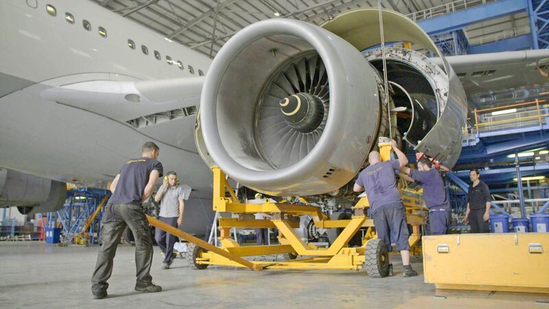 Um das Triebwerk auseinandernehmen und untersuchen zu können, wird die Turbine auf einen Hubwagen geladen. Etwa 70 Arbeiter hantieren gleichzeitig am A330–300. – Bild: Maximus Film GmbH