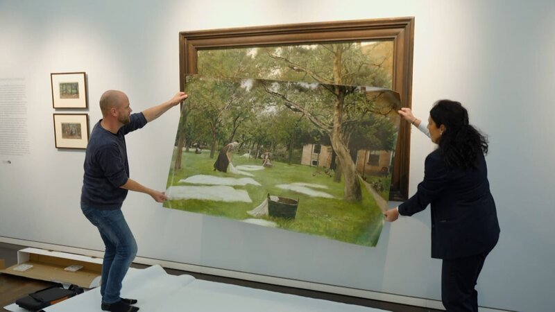 Tim Ernst vergleicht die Reproduktion, die ihm als Vorlage dient mit dem Originalwerk „die Rasenbleiche“ von Max Liebermann. – Bild: ZDF und Tom Kreyssig.