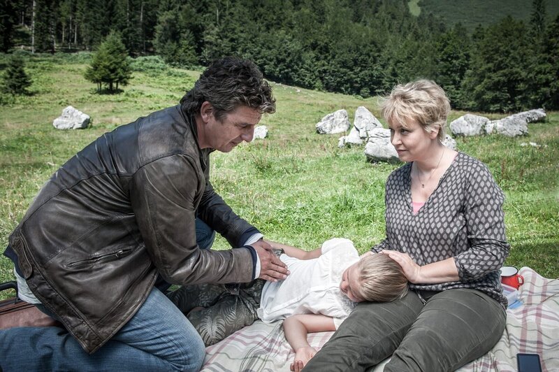 Die kleine Emma Grainer (Hedda Erlebach, M.) ist bei einem Picknick ohnmächtig geworden. Ihre besorgte Mutter (Floriane Daniel, r.) hofft, das Dr. Gruber (Hans Sigl, l.) helfen kann. – Bild: ORF/​ZDF/​Stefanie Leo