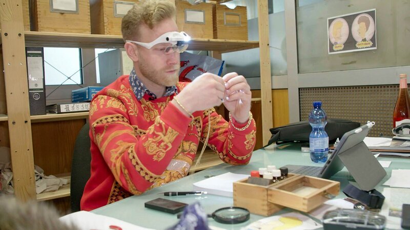 Ep6 – Axel inspecting a gold chain with a pendant. – Bild: Warner Bros. Discovery, Inc. or its subsidiaries and affiliates