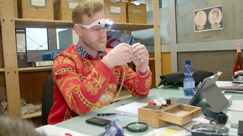 Ep6 – Axel inspecting a gold chain with a pendant. – Bild: Warner Bros. Discovery, Inc. or its subsidiaries and affiliates.