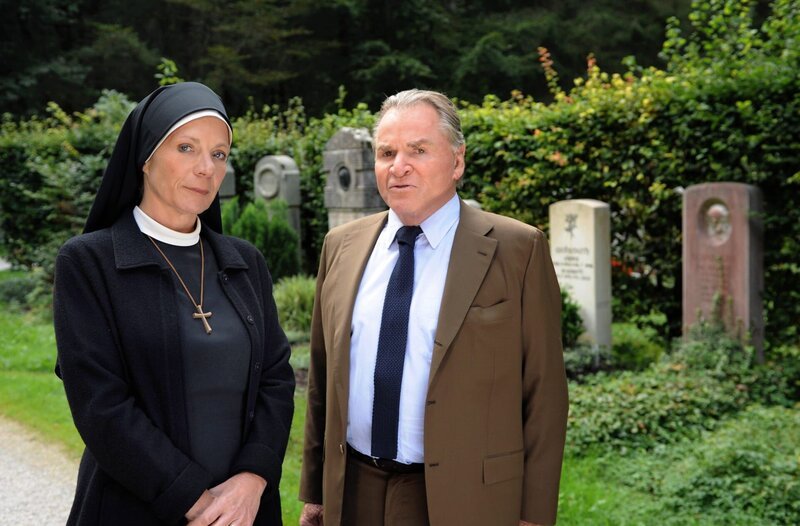Staffel 14: Schwester Theodora (Nina Hoger, l.) trifft Wöller (Fritz Wepper, r.) auf dem Friedhof und will mit ihm über den Kaufvertrag für das Kloster sprechen. – Bild: ARD/​Barbara Bauriedl