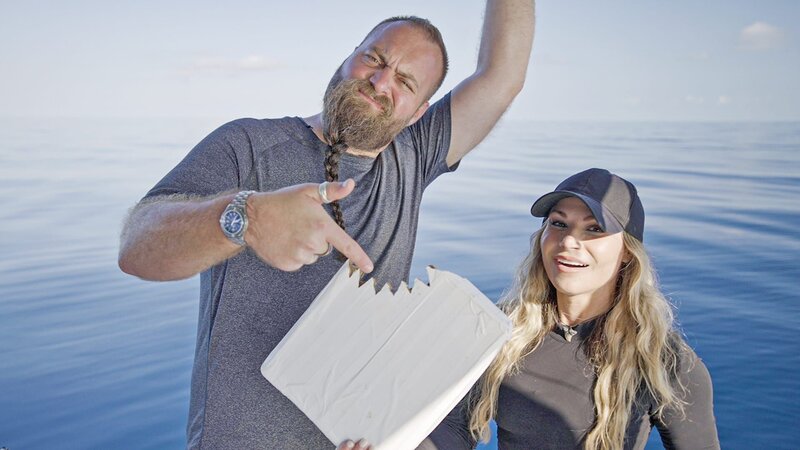 Ein schockierter Tom Hird und Tracy Fanara posieren mit dem vom Hai gebissenen Karton. – Bild: Warner Bros. Discovery, Inc.