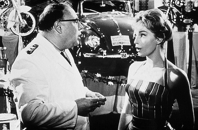 Karin (Maria Perschy) schiebt ihrem Vater Eberhard (Heinz Erhardt) das Gewinnlos der Polizeitombola zu: ein VW Cabriolet. – Bild: VOX Film- und Fernseh-GmbH Karin (Maria Perschy) schiebt ihrem Vater Eberhard (Heinz Erhardt) das Gewinnlos der Polizeitombola zu: ein VW Cabriolet. – Bild: VOX Film- und Fernseh-GmbH
