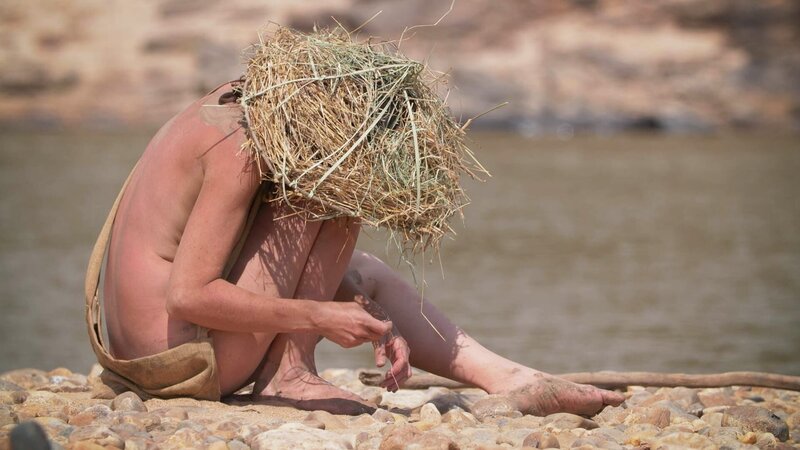 Eine der Survalistas sitzt an einem felsigen Ufer. – Bild: Warner Bros. Discovery