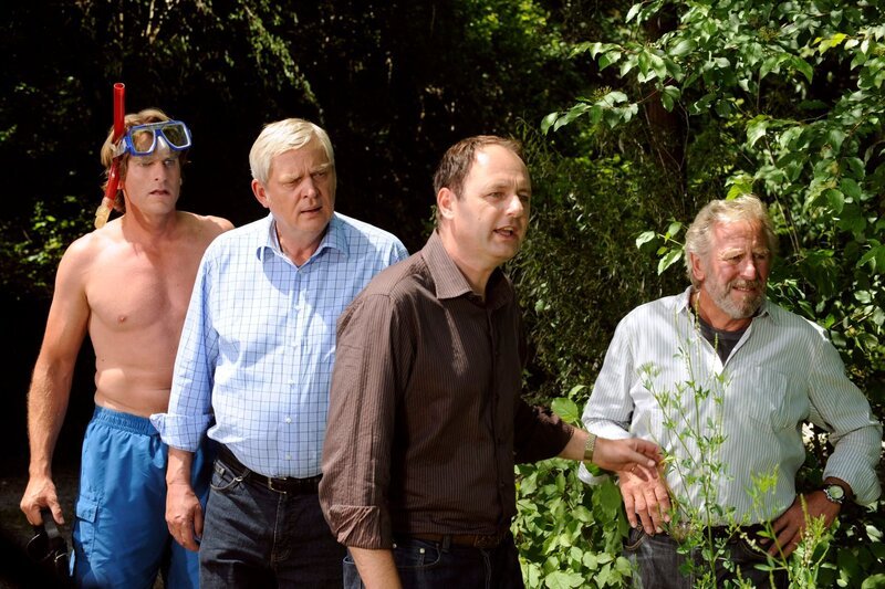 Hubert und die anderen sind erschrocken, als sie einen Taucher aus dem Lansinger See kommen sehen, der offensichtlich ebenfalls auf Schatzsuche war. Von links: Sebastian Wildner (Herbert Ulrich), Joseph Brunner (Wilhelm Manske), Hubert (Bernhard Ulrich) und Martin Kirchleitner (Hermann Giefer). – Bild: BR /​ Marco Orlando Pichler