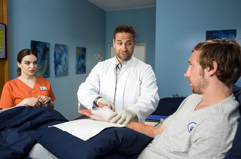 Dr. Moreau (Mike Adler, M.) schaut nach der OP noch einmal nach seinem Patienten Julian Schwarz (Moritz Leu, r.). Jasmin Hatem (Leslie-Vanessa Lill, l.) assistiert. – Bild: ARD/​Daniela Incoronato