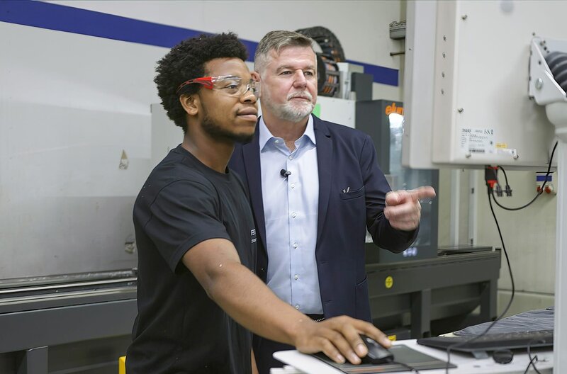 Der Unternehmer Reiner Rudolphi (r.) bespricht sich mit seinem Auszubildenden Jean de Dieu Iradukunda. – Bild: SWR/​Kelvinfilm/​Julia Wolf