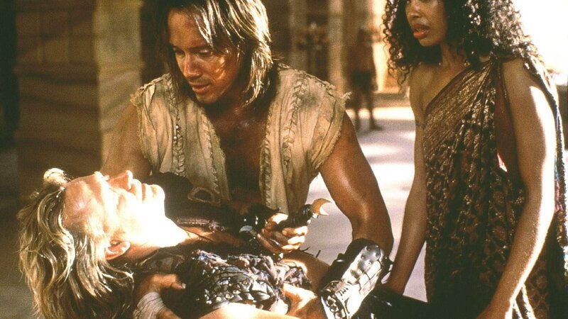 Der böse Dämon Dahak hat einen Dolch zum Schweben gebracht, der eigentlich Nebula (Gina Torres, re.) treffen sollte. Doch Iolaus (Michael Hurst, lieg.), der Nebula retten wollte, wird von dem Dolch durchbohrt. Wird er in Hercules (Kevin Sorbo) Armen sterben? – Bild: TVNOW