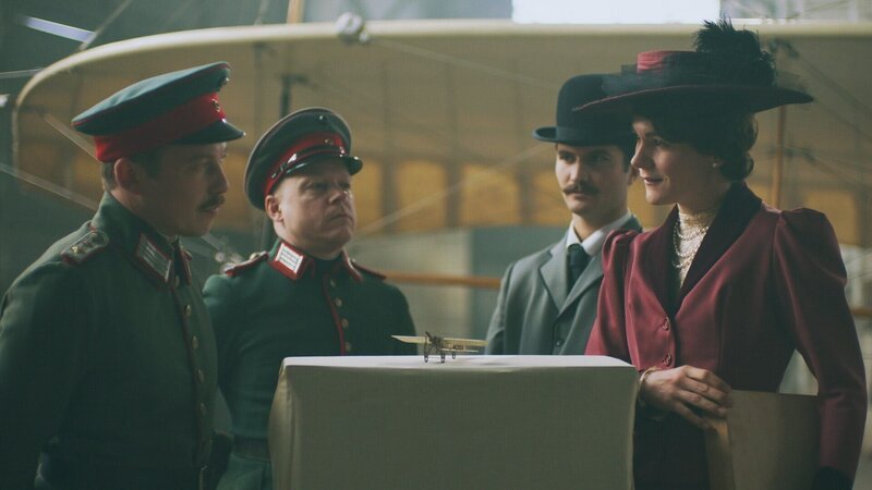 Melli Beese präsentiert dem Militär ihren Prototyp als Flugzeugmodell, (v.l.n.r) Ingo Paulick als Wagenführ, Tanguy Sanglier als Charles Boutard und Lilith Häßle als Melli Beese. – Bild: ORF/​METAFILM