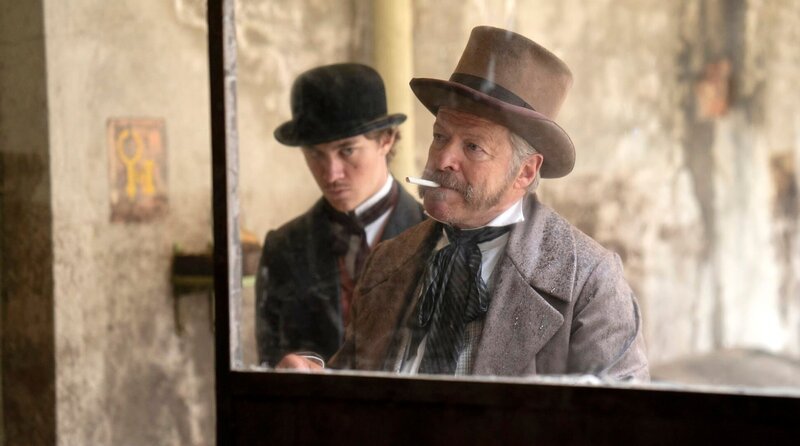 Der Patron J. C. Eddy (Roland Koch, re.) und Sohn Henry (Alessandro Schuster, li.) treiben das Schutzgeld ein. – Bild: ARD Degeto Film/​Lieblingsfilm Produkion GmbH/​Martin Rattini