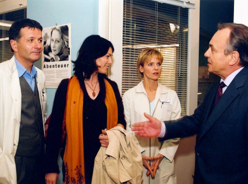 Kathrin (Andrea Kathrin Loewig, 2.v.r.) traut ihren Ohren nicht, als Prof. Simoni (Dieter Bellmann, rechts) und Roland Heilmann (Thomas Rühmann, links) die dreiste Patientin Elena Eichhorn (Cheryl Shepard) als ihre neue Kollegin vorgestellt wird. – Bild: MDR/​Krajewski
