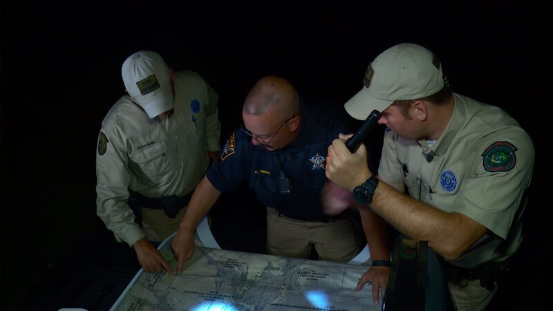 Trent Marker, Mike Stephens, and a Sherif look at a map with flashlights. – Bild: DMAX