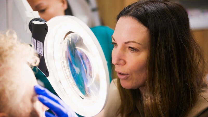 CU shot of Dr Emma looking through the magnifying glass to examine Kate’s face – Bild: Warner Bros. Discovery
