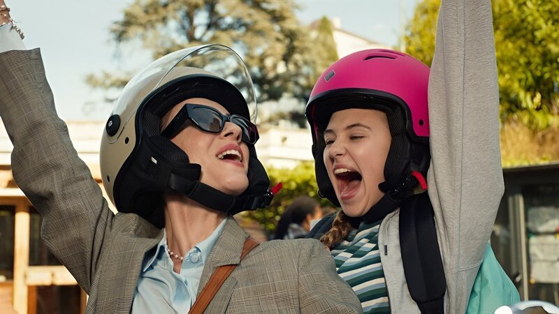 Lucy und ihre Stiefmutter fahren auf einem Roller durch Rom. – Bild: hr/​Red Monk Studios srl/​HSR S1 (FGM) Inc.