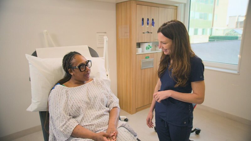 Wide shot Dr Emma smiling at Kyla P, sat on examination bed during consultation. Kyla smiles back. – Bild: Warner Bros. Discovery, Inc.