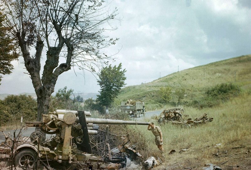 „Ein zerstörter deutscher Transport markiert den Rückzug aus Rom, 18. Juni 1944 Ein britischer Soldat untersucht ein zerstörtes deutsches 88-mm-Geschütz nördlich von Rom. Im Hintergrund fährt ein amerikanischer Lastwagen vorbei. – Bild: THE HISTORY CHANNEL /​ © WildBear Entertainment 2023
