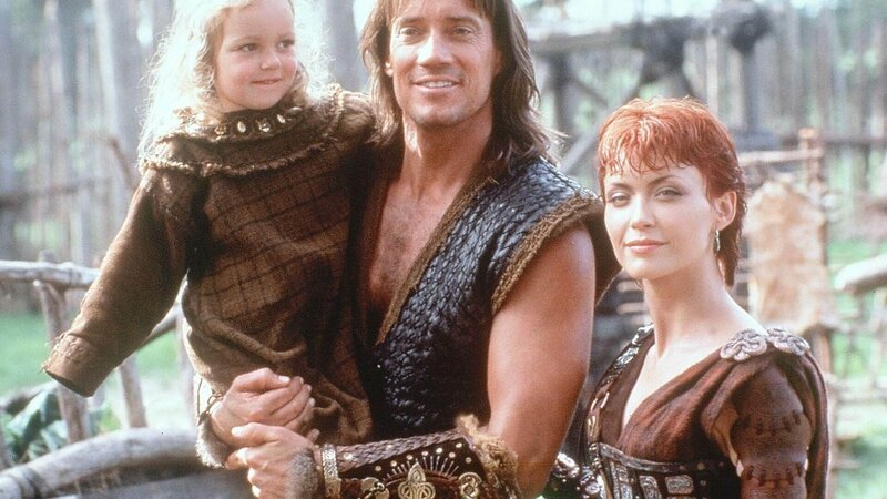 Morrigan (Tamara Gorski, re.) versucht Hercules (Kevin Sorbo) zu überreden, noch eine Weile bei ihr und ihrer Tochter Brigid (Benedicta Joseph) zu bleiben, um herauszufinden, ob er sich ein gemeinsames Leben mit ihr in Irland vorstellen kann. – Bild: TVNOW
