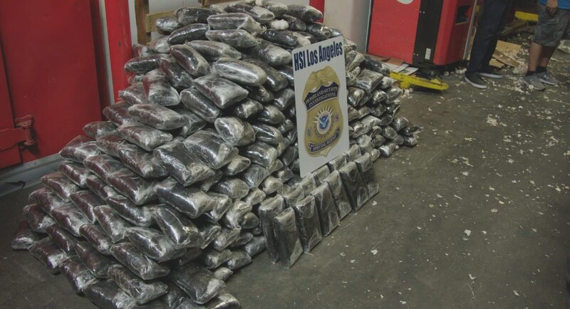 Packages of suspected narcotics found within boxes of garlic stacked behind an HSI Los Angeles sign. – Bild: National Geographic