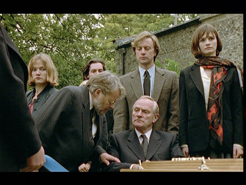 Auf der Beerdigung der ermordeten Emily Simpson ist halb Badger’s Drift versammelt: Judy Lessiter (Jessica Stevenson, l.), Dr. Trevor Lessiter (Bill Wallis, 2.v.l.), Gutsbesitzer Henry Trace (Julian Glover, M. sitzend), der Gutsverwalter David Whitely (Christopher Villiers, 2.v.r.) sowie die zukünftige Mrs. Trace, Katherine Lacey (Emily Mortimer, r.). Doch ist die Trauer wirklich echt? – Bild: Bentley Production