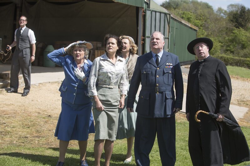 Vorne: Mrs McCarthy (Sorcha Cusack, l.), Meg Le Broc (Leah Whitaker, 2.v.l.), Lady Felicia (Nancy Carroll, M.), Arthur Le Broc (Rupert Vansittart, 2.v.r.) und Father Brown (Mark Williams, r.) müssen tatenlos dabei zusehen, wie Ned mit seiner Tochter durch die Lüfte fliegt. – Bild: ZDF und Gary Moyes