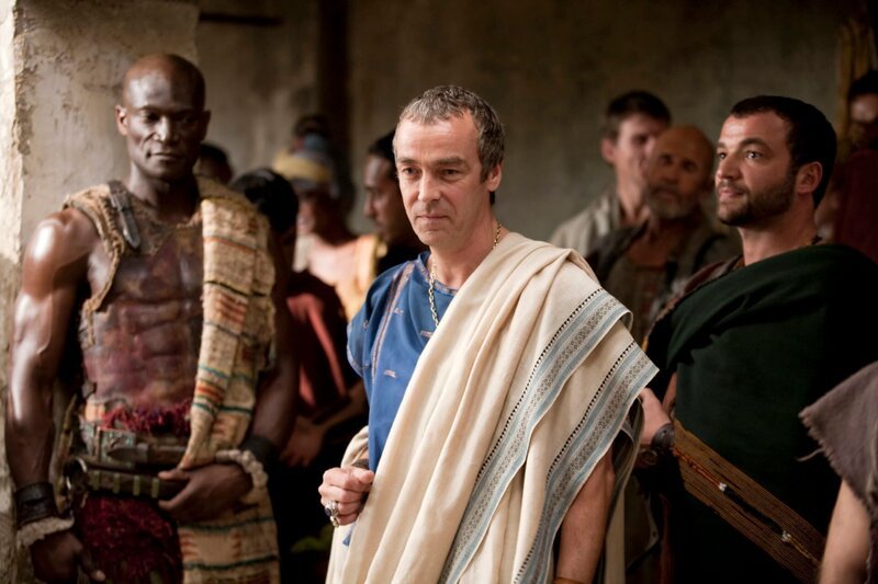 Während Spartacus einen Kampf nach dem anderen gewinnt, machen sich Batiatus (John Hannah, M.), Drago (Peter Mensah, l.) und Ashur (Nick Tarabay, r.) auf, um am Sklavenmarkt neue Sklaven zu ergattern … – Bild: Starz Entertainment, LLC