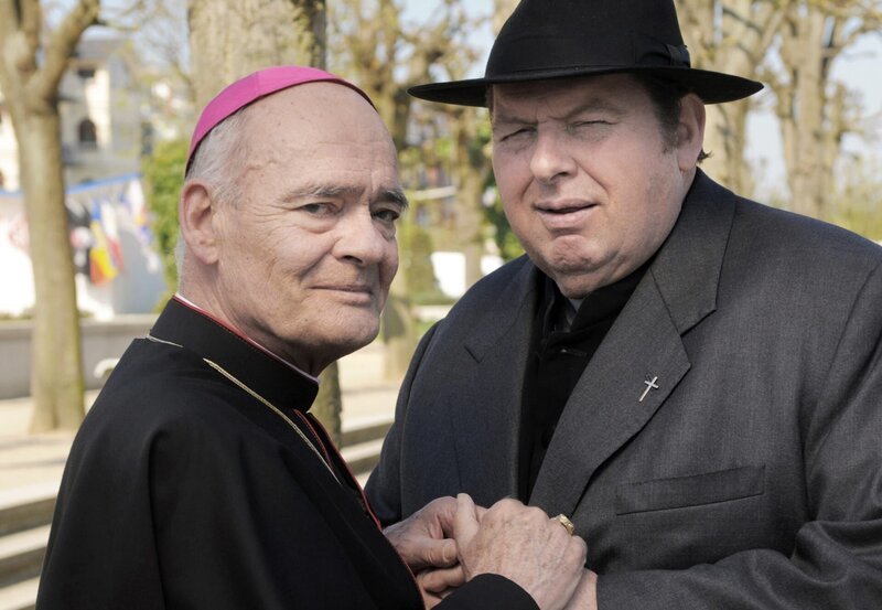 Bischof Hemmelrath (Hans-Michael Rehberg, links) dankt Pfarrer Braun (Ottfried Fischer). – Bild: ARD Degeto/​Reiner Bajo