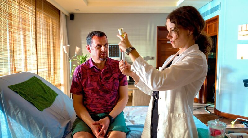 Hotelärztin Filipa (Anja Knauer) behandelt den Hotelgast Karli (Gerhard Wittmann). – Bild: ARD Degeto/​BR/​Tivoli Film/​Diensen Pamben