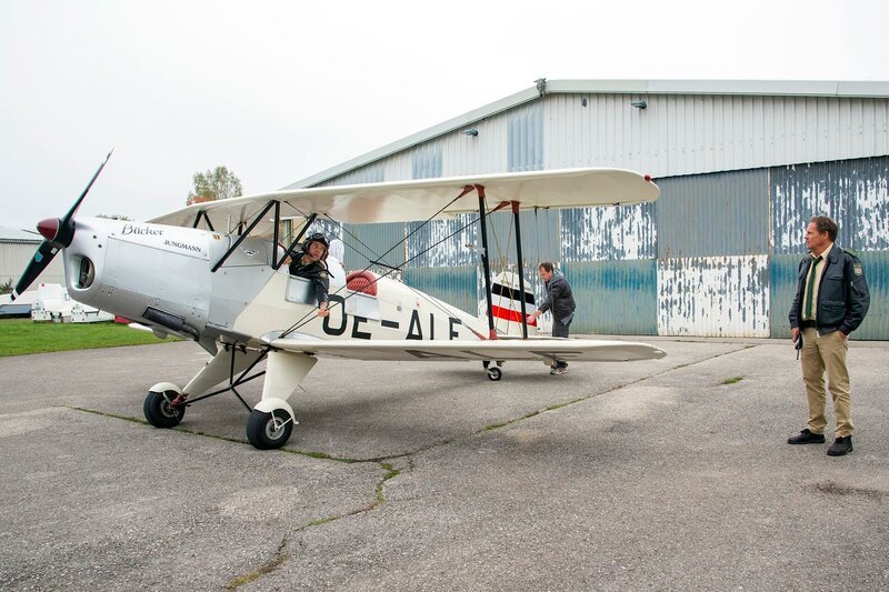 Staller (Helmfried von Lüttichau, l.) muss zwecks Spurensuche einen Rundflug im Doppeldecker über sich ergehen lassen. V.l.n.r. Staller (Helmfried von Lütichau), Flugschulleiter Michael Kronthaler (Chrisitian Heiner Wolf), Hubert (Christian Tramitz). – Bild: ARD/​TMG/​Marco Meenen