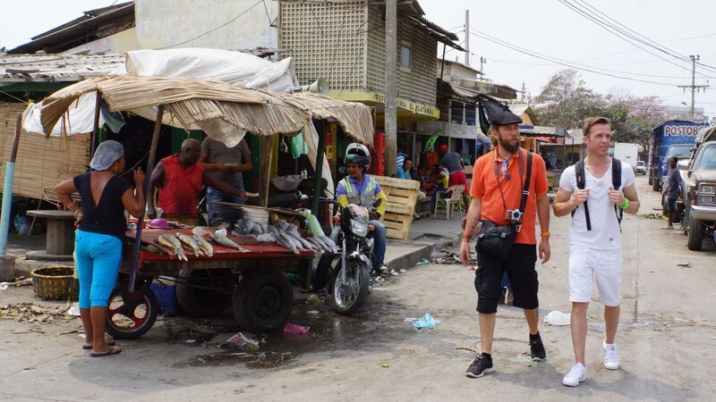 Zauberer Kalibo und Entertainment-Manager Alex laufen durch die Marktstraße in Cartagena, Kolumbien, an einem Fischstand vorbei – Bild: BR/​Deborah Stöckle